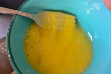 A person holding a spoon over a bowl of eggs
