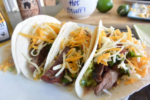Three tacos with cheese, meat and salsa on a plate