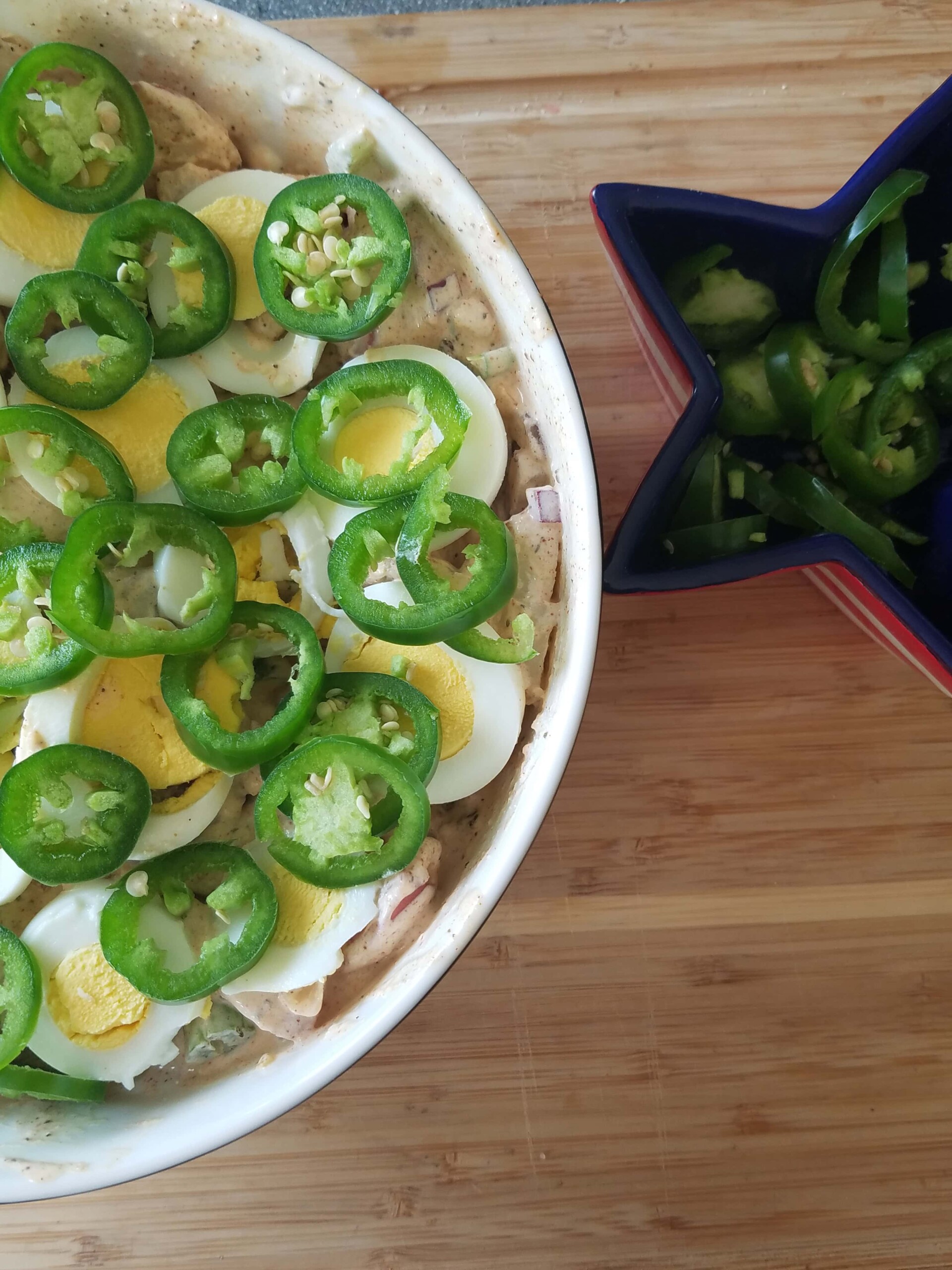 A bowl of potato salad with eggs and jalapenos 