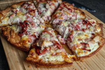 A pizza with ham and cheese on a wooden cutting board