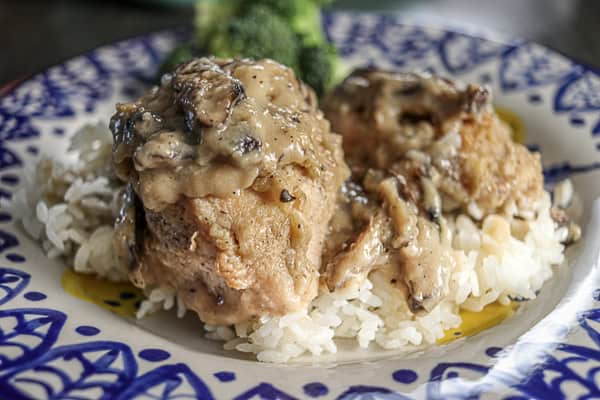 Chicken thighs with a mushroom gravy and broccoli on a white plate