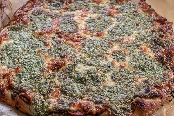 A pizza with pesto on top on a wooden cutting board