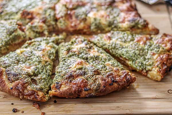 A pizza with pesto on it sitting on a cutting board