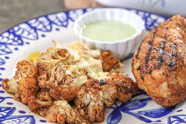 A grilled chicken breast with roasted cauliflower and a side of creamy sauce
