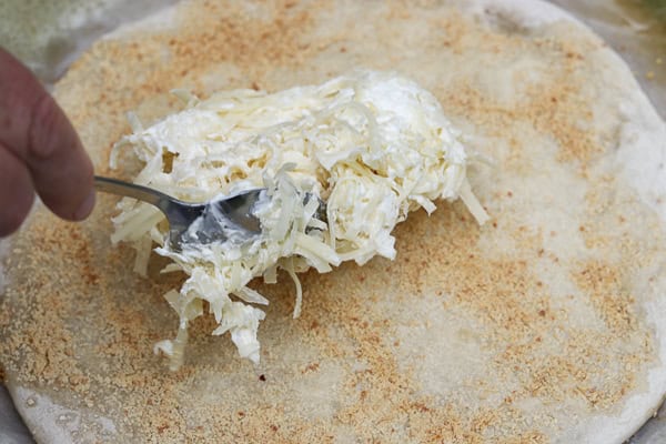A person is using a spoon to spread cheese on a pizza