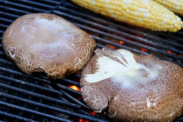 Two mushrooms on a grill with corn on the cob