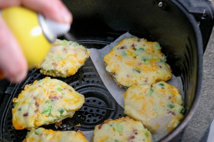 Potato cakes in air fryer being sprayed with cooking spray