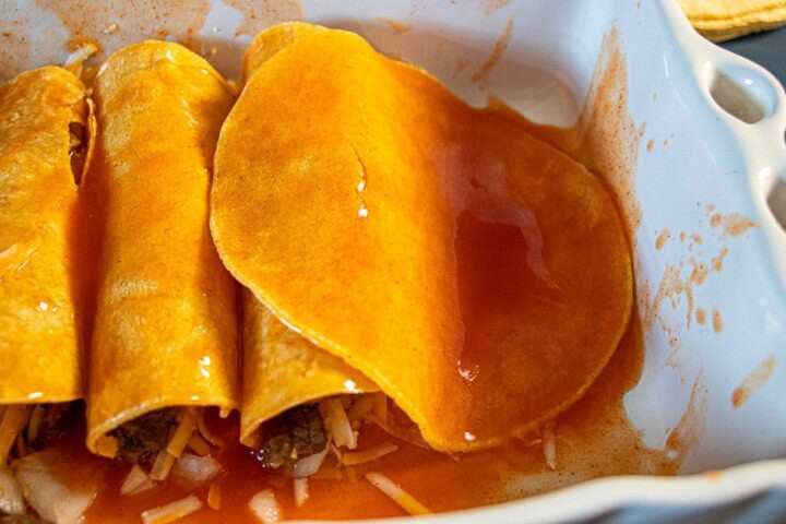 Tortilla dipped in sauce in a casserole dish