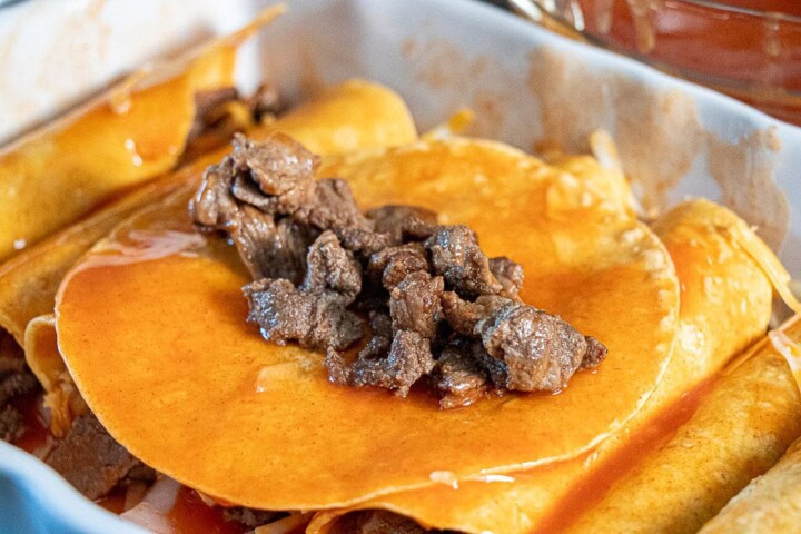 Tortilla dipped in sauce in a casserole dish with steak