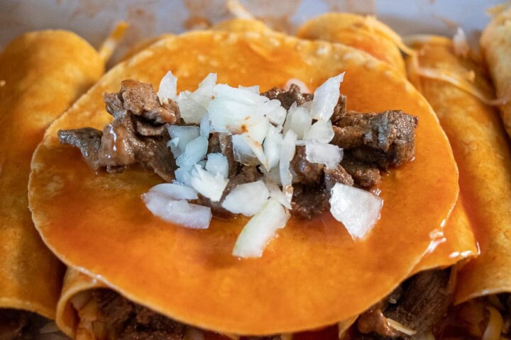Tortilla dipped in sauce in a casserole dish with steak and onion