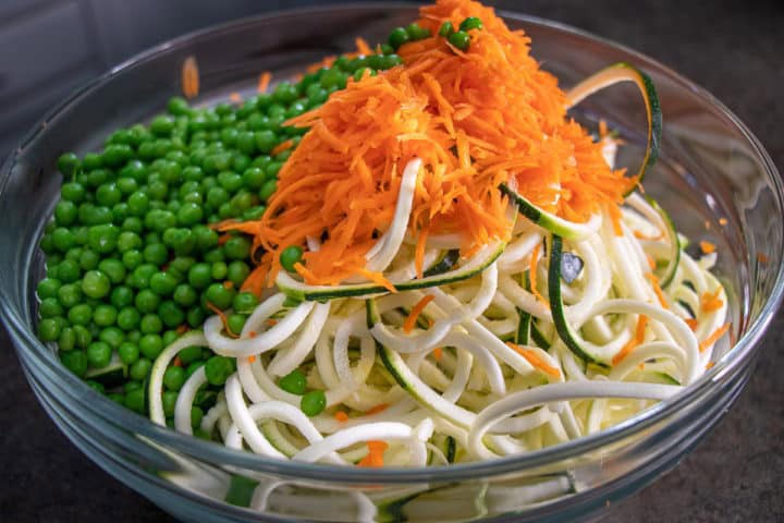 A bowl of noodles, carrots, peas and carrots