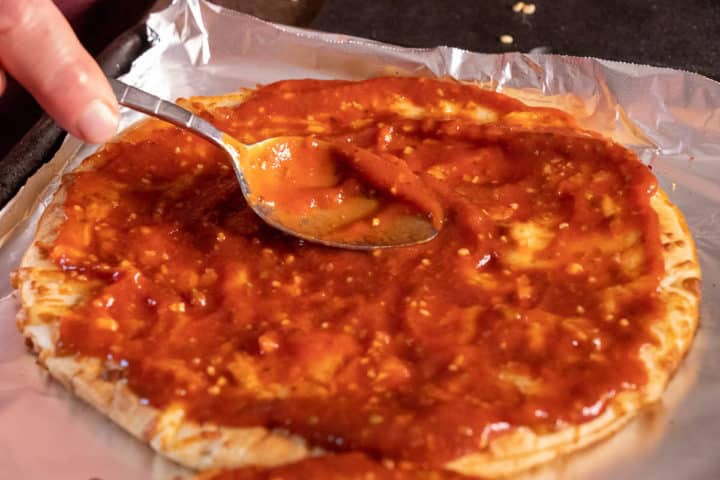 Sauce on pizza crust with a spoon