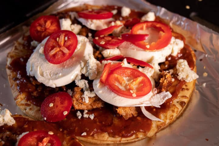 Sauce on pizza crust with sausage and cheese, topped with peppers
