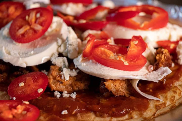 Sauce on pizza crust with sausage and cheese, topped with peppers