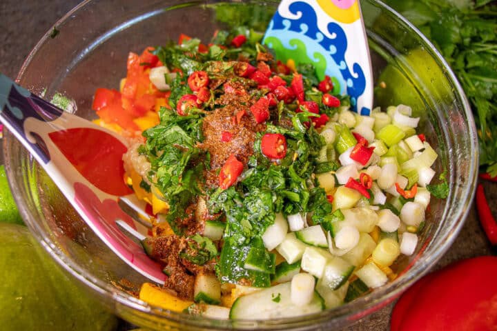 Chopped Mango, cucumber, peppers, and Cilantro in a bowl with spoons