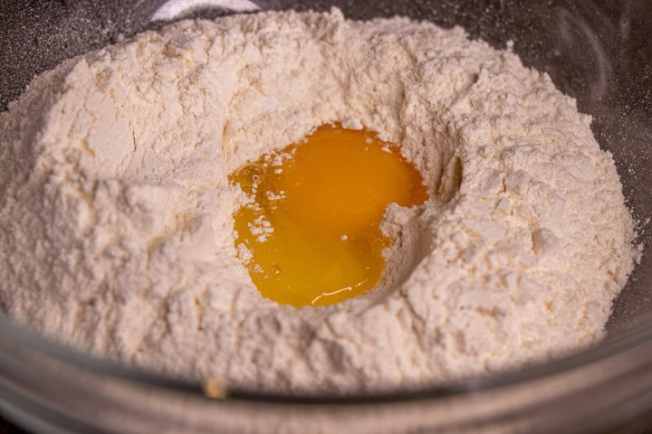 An egg is in a bowl of flour and sugar