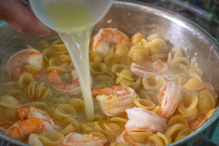 Lemon juice pouring into a pan with Shrimp and pasta