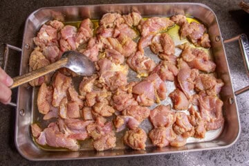 Chicken thighs in a roasting pan with a spoon